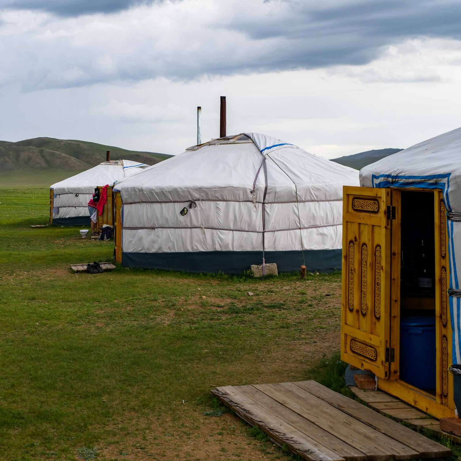 Traditional Mongolian gers on open grassland beneath low hills, with one carved wooden door standing open